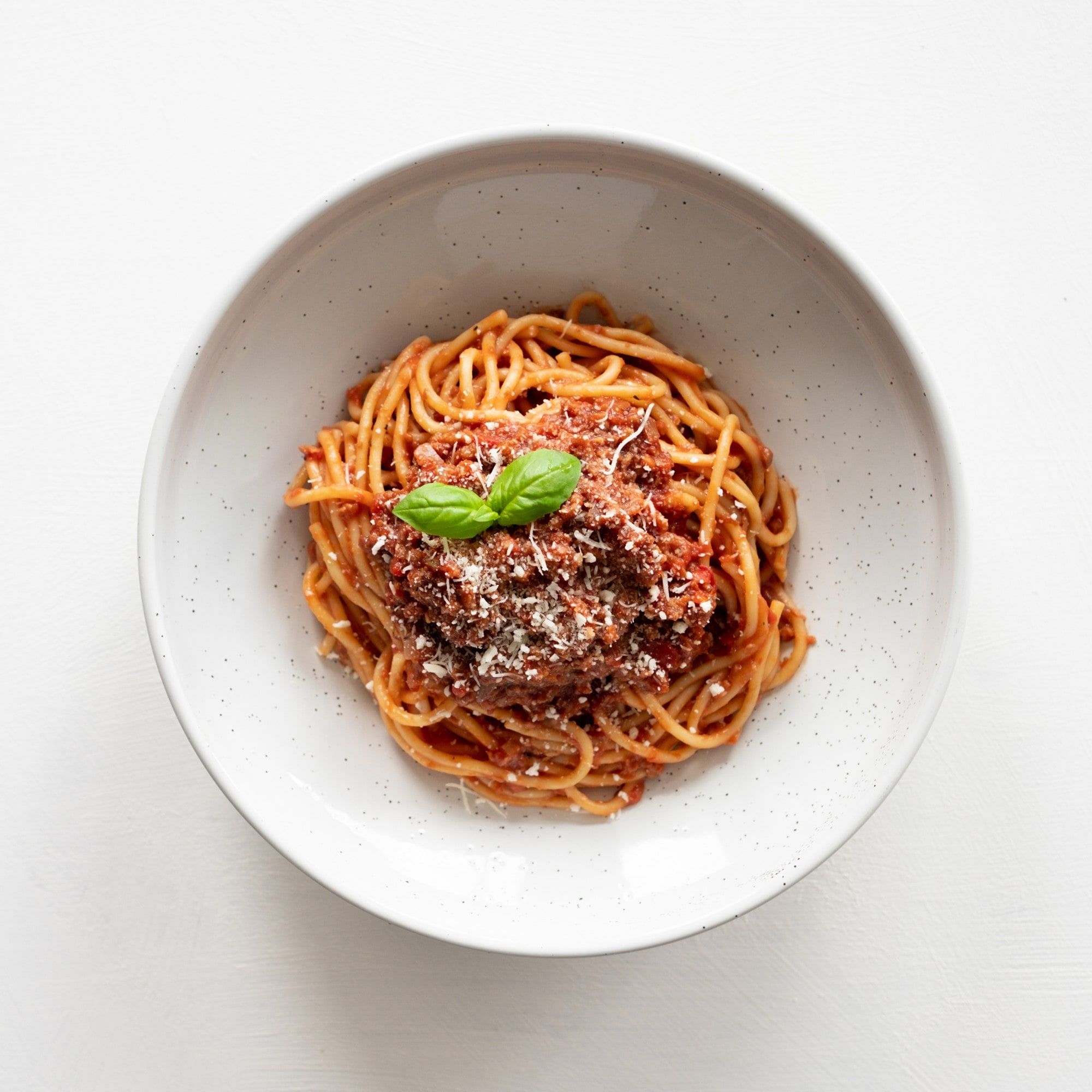 A bowl of spaghetti bolognese topped with basil and grated cheese.